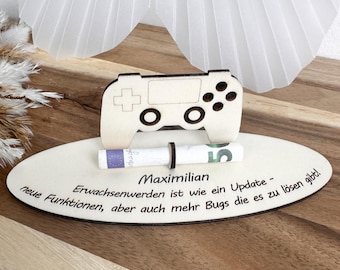 May include: A wooden game controller-shaped money holder with a rolled-up bill secured by a black band. The holder sits on an oval wooden base with the name "Maximilian" and a German quote. The design is light-colored.