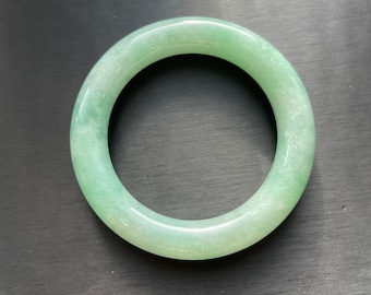 May include: A light green jade bangle bracelet. The bangle is smooth and polished.