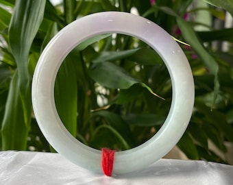 May include: A light green jade bangle with a lavender hue. The bangle is smooth and polished, and it is tied with a red string.