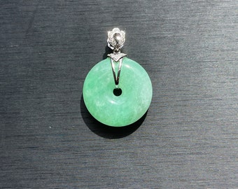May include: A green jade pendant in the shape of a circle with a hole in the center. The pendant is attached to a silver chain with a diamond-encrusted bail.