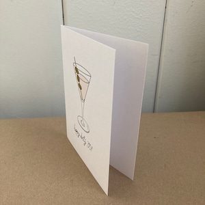 May include: A white card with a black line drawing of a martini glass with three olives on a toothpick. The text "Happy dirty 30!" is written below the glass.