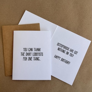 May include: A white greeting card with the text "YOU CAN THANK THE DAIRY LOBBYISTS FOR ONE THING..." is next to an open card that reads "OSTEOPOROSIS HAS GOT NOTHING ON YOU! HAPPY BIRTHDAY!". A brown envelope is visible.