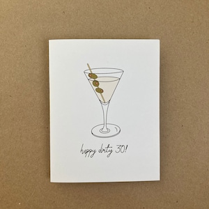 May include: A white card with a black line drawing of a martini glass with three green olives on a stick. The text "happy dirty 30!" is written below the glass.