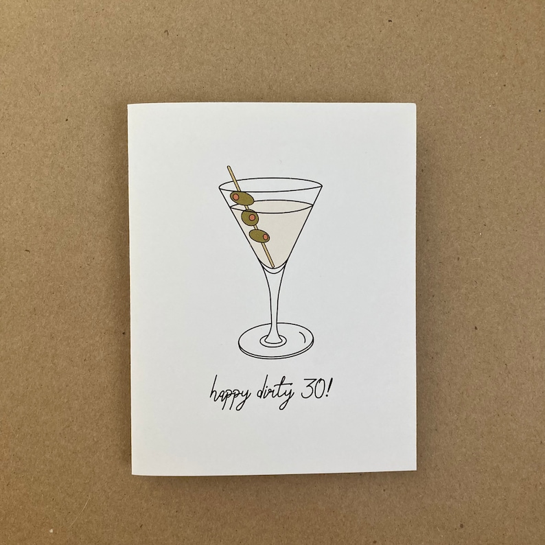 May include: A white card with a black line drawing of a martini glass with three green olives on a stick. The text "happy dirty 30!" is written below the glass.
