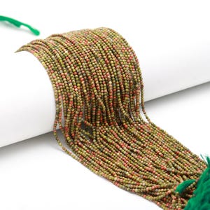 May include: A strand of green, red and brown gemstone beads. The beads are small and round, and they are strung together on a thin thread. The beads are all different sizes and shapes, and they have a natural, earthy look.