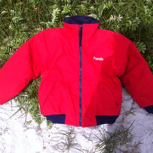 Könnte beinhalten: Rote Fleecejacke mit schwarzem Reißverschluss und dunkelblauem Besatz. Die Jacke hat das Wort "Panda" auf der Vorderseite gestickt.