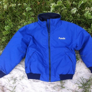 Può includere: Una giacca in pile blu con fodera blu scuro e un logo ricamato bianco che dice "Panda".