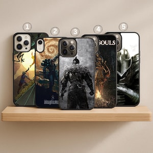May include: A collection of five phone cases with various designs. The cases feature artwork with themes of fantasy and gaming. The cases are black with images of characters, landscapes, and text. The cases are displayed on a wooden shelf.