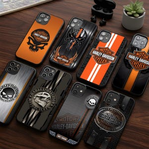 May include: A collection of Harley-Davidson phone cases in various designs. The cases feature skull graphics, the Harley-Davidson logo, and orange and black color schemes. Some cases have stripes or textured patterns.