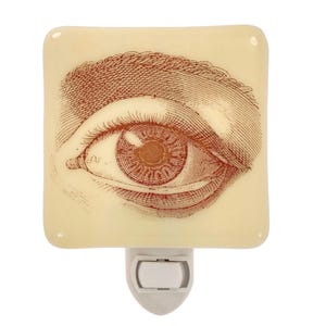 May include: A decorative night light featuring a detailed, sepia-toned illustration of a human eye. The eye is set against a square, off-white background. The night light has a standard plug-in base.