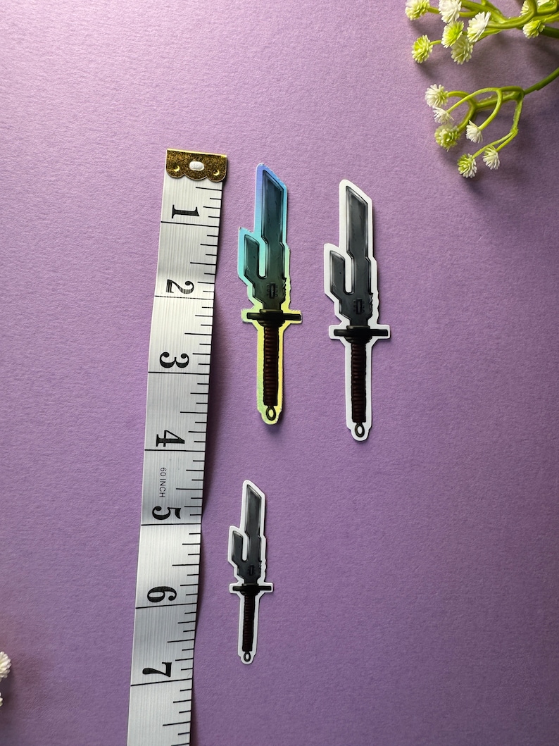 May include: Three stickers of pixelated swords with a rainbow gradient. The swords are on a purple background with a ruler for scale.