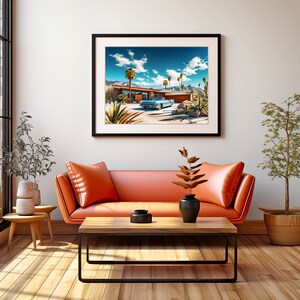 May include: A framed print of a mid-century modern home with a blue car parked in the driveway. The home is surrounded by palm trees and desert landscaping. The print is hanging on a white wall in a living room setting with an orange couch and a coffee table.