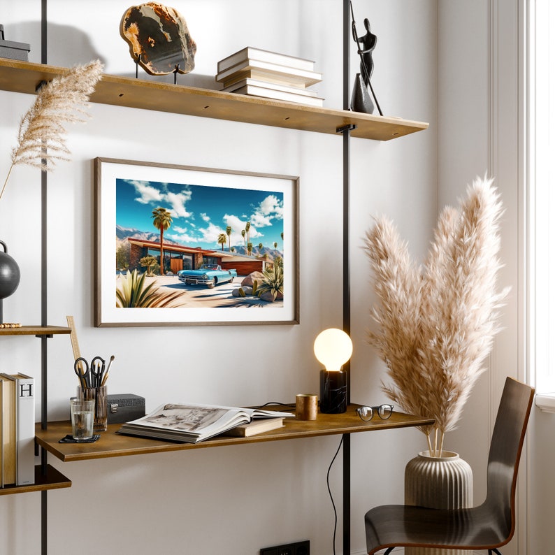 May include: A framed print of a mid-century modern home with a blue car parked in the driveway. The home is surrounded by palm trees and a blue sky with white clouds. The print is hanging on a wall with a wooden shelf above it.