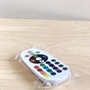 May include: White remote control with a circular button in the center labeled "W" for white light. The remote has buttons for red, green, blue, and other color options. The remote is in a clear plastic bag.