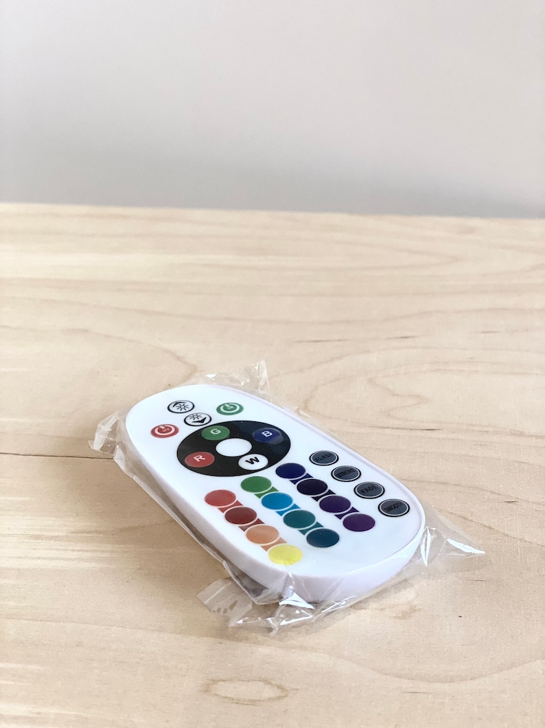 May include: White remote control with a circular button in the center labeled "W" for white light. The remote has buttons for red, green, blue, and other color options. The remote is in a clear plastic bag.