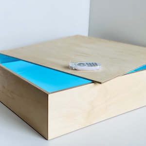 May include: A wooden box with a light blue interior and a removable lid. A white remote control is on top of the lid.