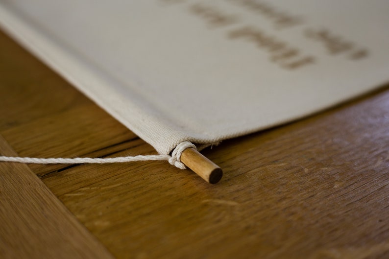 May include: A close-up of a white canvas banner with a wooden dowel rod at the bottom. The banner is attached to the dowel rod with a white string.