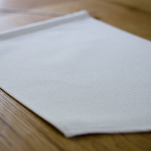 May include: A plain white fabric banner with a slightly textured surface. The banner is hanging on a wooden surface.