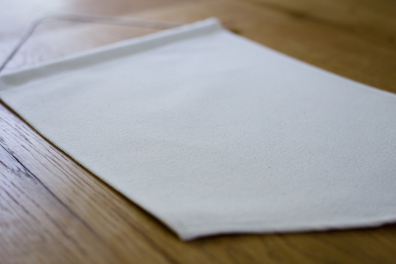 May include: A plain white fabric banner with a slightly textured surface. The banner is hanging on a wooden surface.