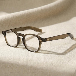 May include: Round-framed spectacles in a translucent brown hue. The glasses feature a classic keyhole bridge and delicate detailing on the arms. The clear lenses are set in a sturdy frame, offering a timeless aesthetic. The frame is approximately 14 cm wide.