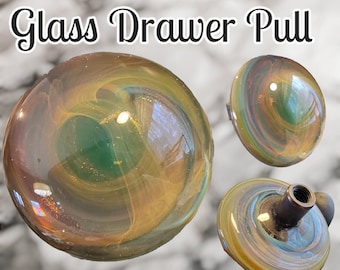 May include: A glass drawer pull with a swirling pattern of green, gold, and brown. The pull is 1 5/8 inches in diameter.