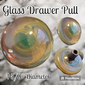 May include: A glass drawer pull with a swirling pattern of green, gold, and brown. The pull is 1 5/8 inches in diameter.