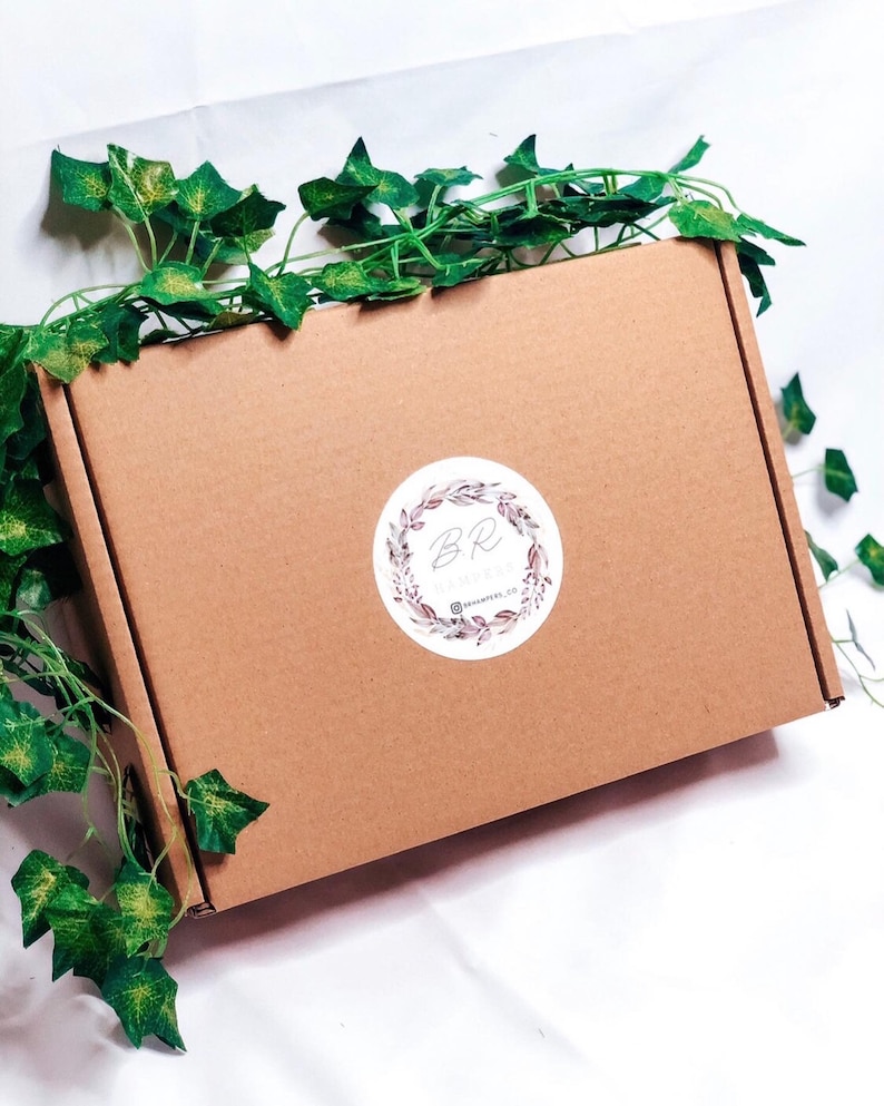 May include: A brown cardboard box with a circular sticker featuring the letters "BR" surrounded by a floral wreath. Green ivy vines are draped around the box. The sticker also includes the text "@renamers.co".