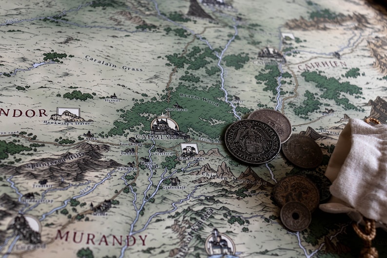 May include: A close-up of a map of the fictional land of Andor, with a small pouch of silver coins on top. The map shows the location of Caemlyn, a city in the fictional world of Andor.