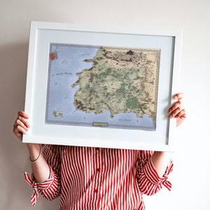 May include: A person holds a framed map of a fictional land with a white frame and a light blue and green map inside. The map is titled "The World of Eldoria".