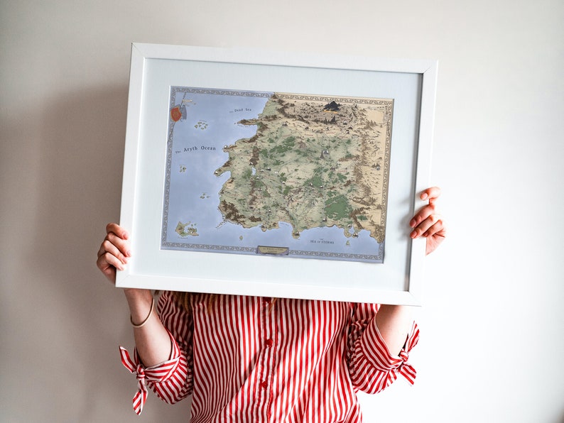 May include: A person holds a framed map of a fictional land with a white frame and a light blue and green map inside. The map is titled "The World of Eldoria".
