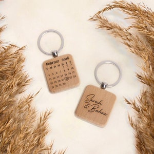 May include: Two wooden keyrings with silver key rings. One keyring features a calendar with the date February 22, 2018, highlighted. The other keyring has the names "Sarah & Bahae" engraved on it.