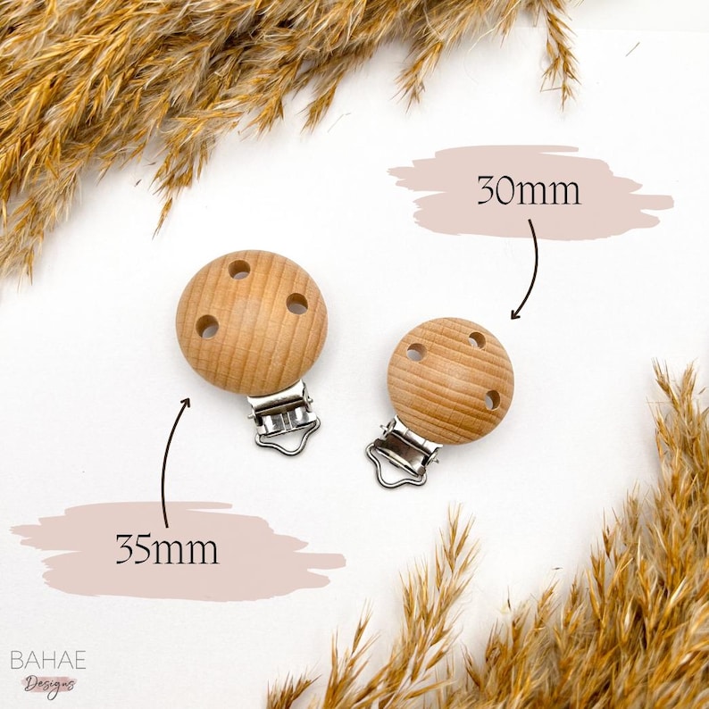 May include: Two wooden baby teether clips, one 30mm and one 35mm, with silver metal clips. The teethers are light brown and have three holes each.