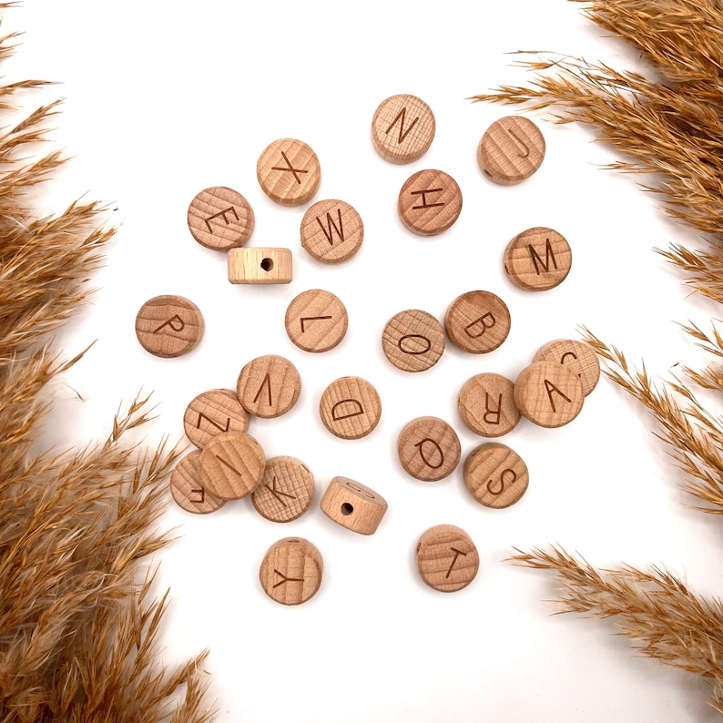 May include: Wooden alphabet beads in various letters, including A, B, C, D, E, F, G, H, I, J, K, L, M, N, O, P, Q, R, S, T, U, V, W, X, Y, and Z. The beads are light brown and have a natural wood finish.