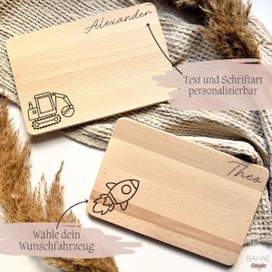 Peut inclure: Deux planches &agrave; d&eacute;couper rectangulaires en bois avec des motifs grav&eacute;s. L'une pr&eacute;sente une excavatrice et le nom "Alexander", l'autre une fus&eacute;e et le nom "Theo". Le texte sur l'image dit "Texte et police personnalisables" et "Choisissez votre v&eacute;hicule souhait&eacute;".