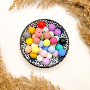 Puede incluir: Un bol lleno de cuentas de silicona de colores. Las cuentas son de varios tonos de rosa, azul, verde, amarillo y rojo. Las cuentas est&aacute;n en un bol blanco con un patr&oacute;n floral.