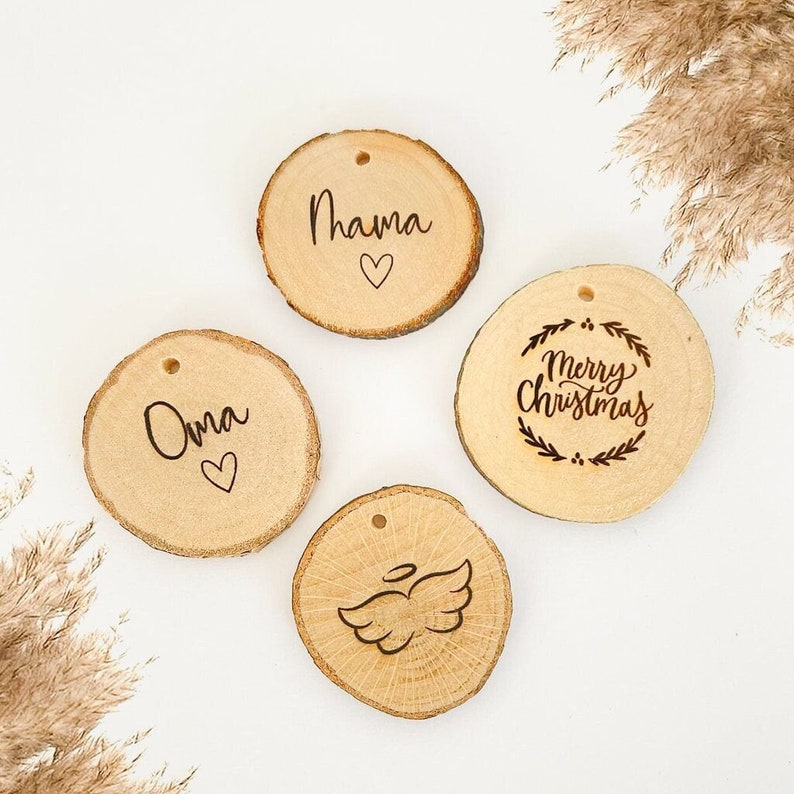 May include: Four round wooden ornaments with different designs. One ornament says "Merry Christmas" in a wreath, another says "Oma" with a heart, another says "Mama" with a heart, and the last one has an angel wing design.