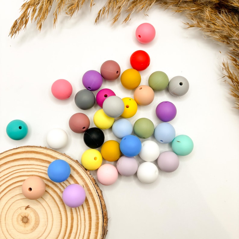 Puede incluir: Una colecci&oacute;n de cuentas de silicona de colores en varios tonos de azul, verde, amarillo, rosa, rojo, morado y gris. Las cuentas est&aacute;n dispuestas en un mont&oacute;n suelto sobre una superficie blanca.