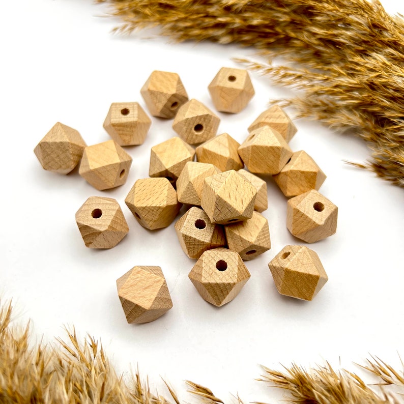 Könnte beinhalten: Eine Gruppe von Naturholzkugeln mit geometrischer, facettierter Form. Die Kugeln haben ein Loch in der Mitte zum Aufziehen.