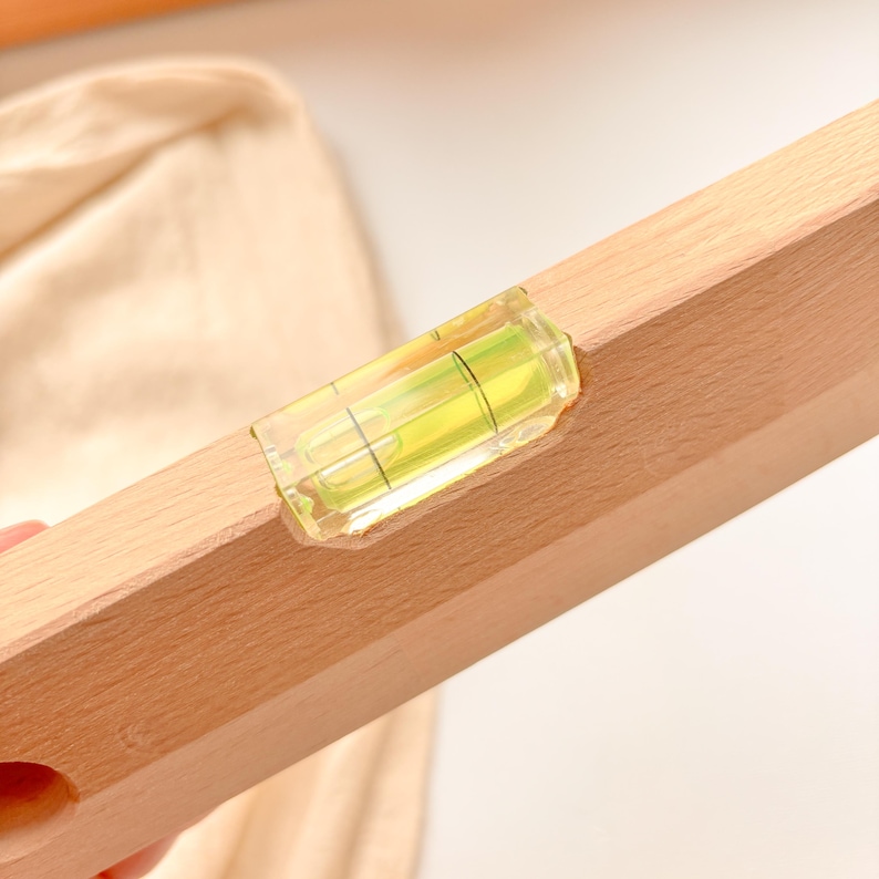 May include: A wooden level with a clear, bubble-filled vial. The level is made of light-colored wood and has a yellow and green liquid inside the vial. The level is designed to help ensure surfaces are straight and even.