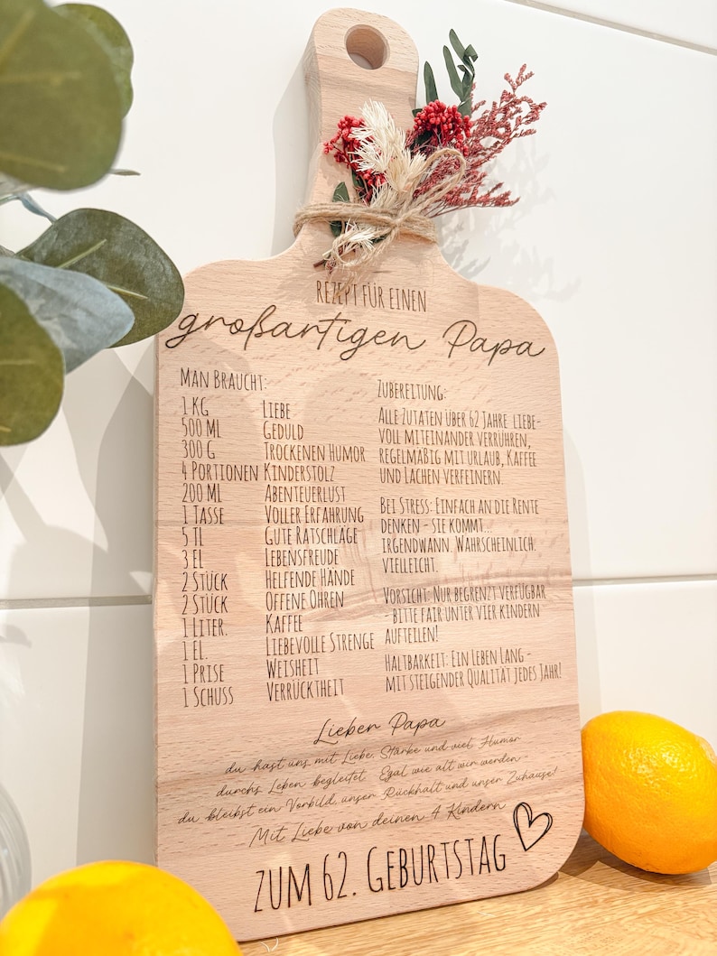 Könnte beinhalten: Holzschneidebrett mit Griff, graviert mit einem Rezept für einen großartigen Papa. Das Brett ist mit Trockenblumen und Bindfaden verziert. Eine Zitrone liegt neben dem Brett. Der Text enthält Maße und Zutaten.