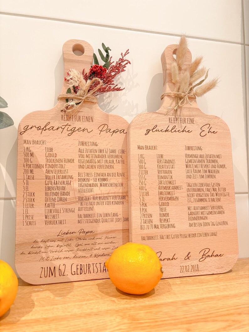 May include: Two wooden cutting boards with engraved recipes, one for a "great Dad" and the other for a "happy marriage." Each board is decorated with dried flowers and tied with twine. A lemon sits in front.