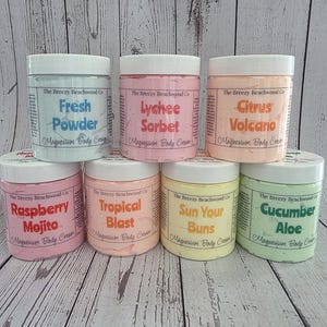 K&ouml;nnte beinhalten: Sieben runde Kunststoffdosen mit Magnesium-K&ouml;rpercreme von The Breezy Beachwood Co. in verschiedenen Pastellfarben. Die D&uuml;fte umfassen Fresh Powder, Lychee Sorbet, Citrus Volcano, Raspberry Mojito, Tropical Blast, Sun Your Buns und Cucumber Aloe.