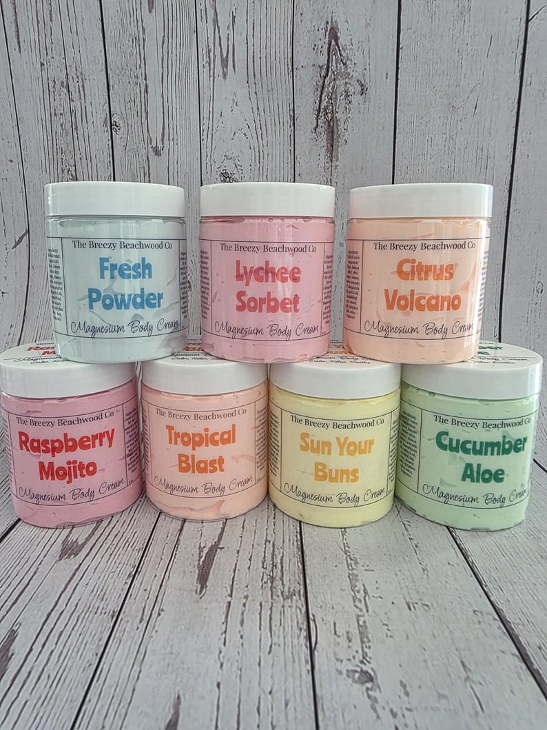 K&ouml;nnte beinhalten: Sieben runde Kunststoffdosen mit Magnesium-K&ouml;rpercreme von The Breezy Beachwood Co. in verschiedenen Pastellfarben. Die D&uuml;fte umfassen Fresh Powder, Lychee Sorbet, Citrus Volcano, Raspberry Mojito, Tropical Blast, Sun Your Buns und Cucumber Aloe.