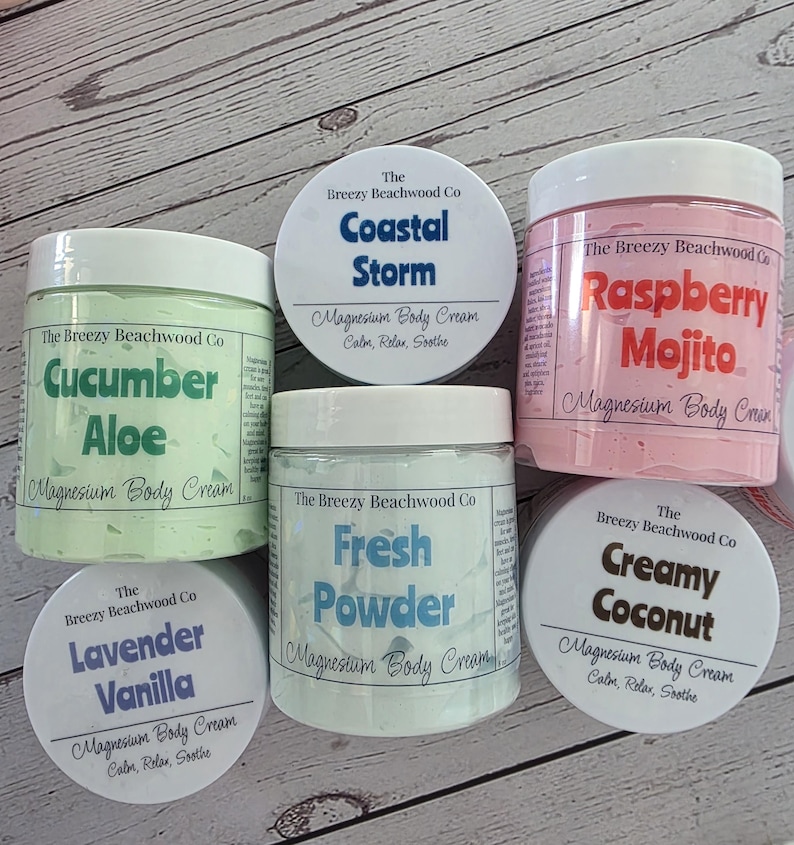 K&ouml;nnte beinhalten: F&uuml;nf runde Kunststoffdosen mit Magnesium-K&ouml;rpercreme von The Breezy Beachwood Co. Die Duftrichtungen umfassen Cucumber Aloe, Coastal Storm, Raspberry Mojito, Fresh Powder, Lavender Vanilla und Creamy Coconut, jeweils mit wei&szlig;en Deckeln.
