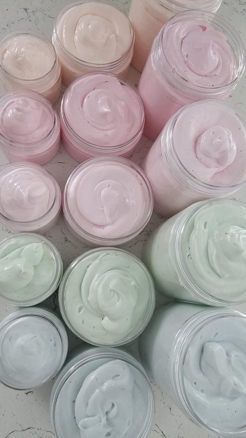 K&ouml;nnte beinhalten: Eine Sammlung von durchsichtigen Kunststoffdosen, gef&uuml;llt mit aufgeschlagener K&ouml;rperbutter in verschiedenen Pastellt&ouml;nen wie Hellrosa, sanftem Pfirsich, Minzgr&uuml;n und Hellblau. Die dicke, cremige Substanz ist in jedem Beh&auml;lter mit sichtbaren Spitzen.