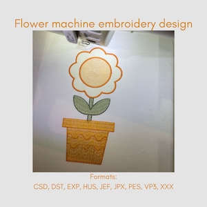 Puede incluir: Diseño de bordado a máquina de una flor amarilla en una maceta amarilla con un tallo y hojas verdes. El diseño está en una tela blanca. Formatos: CSD, DST, EXP, HUS, JEF, JPX, PES, VP3, XXX