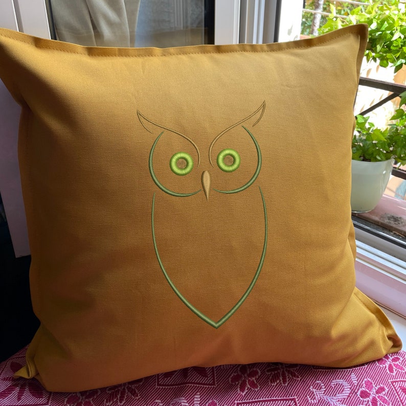 May include: A mustard yellow throw pillow with an embroidered green owl design. The owl has large, round eyes.