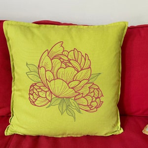 Pu&ograve; includere: Un cuscino quadrato verde lime con un grande design di peonia ricamata in rosa e verde. Il cuscino &egrave; posto su un divano rosso, creando un contrasto cromatico sorprendente. Il motivo floreale aggiunge un tocco di decorazione ispirata alla natura.