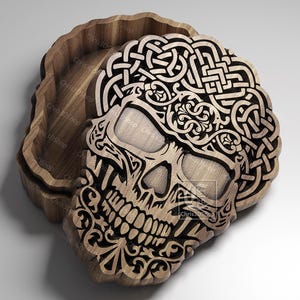 May include: Wooden box with a carved skull design. The skull features intricate Celtic knotwork and floral patterns. The box is made of light-colored wood and has a lid that fits snugly. The CNC logo is visible in the upper left corner.