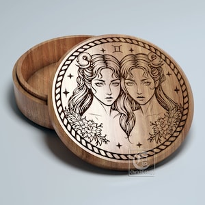 May include: A wooden box with a round lid featuring a laser-engraved design of the Gemini zodiac sign. The design depicts two women with long hair and floral accents. The lid is open, revealing the empty interior of the box.